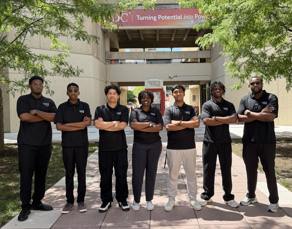 Group of 6 individuals arms crossed in black polos and smiling.