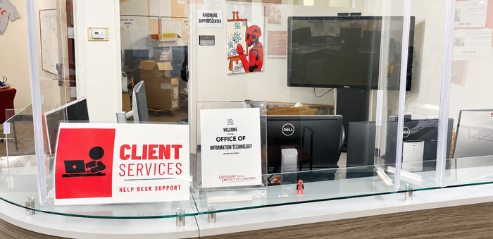 Client services help desk counter behind a glass partition, with computer monitors and a welcome sign for an office of information technology.