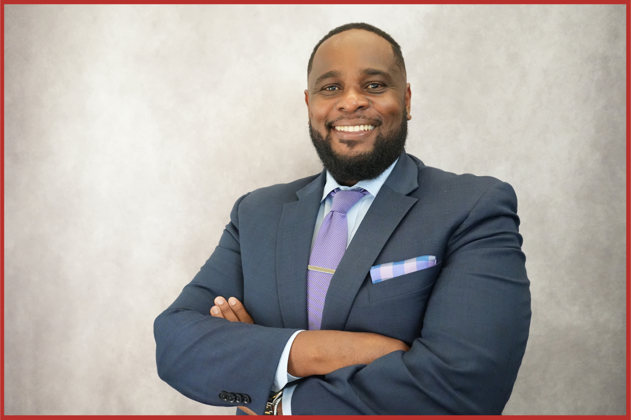 Vice President of Office of Information Technology half body photo in a navy suit, arms crossed and smiling.