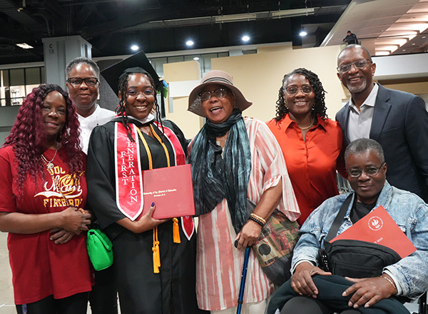 Group of family members posing together at a graduation celebration, with the graduate in cap and gown holding a diploma.