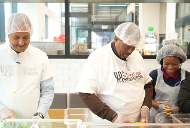 Two men and a young woman smiling and chopping lettuce