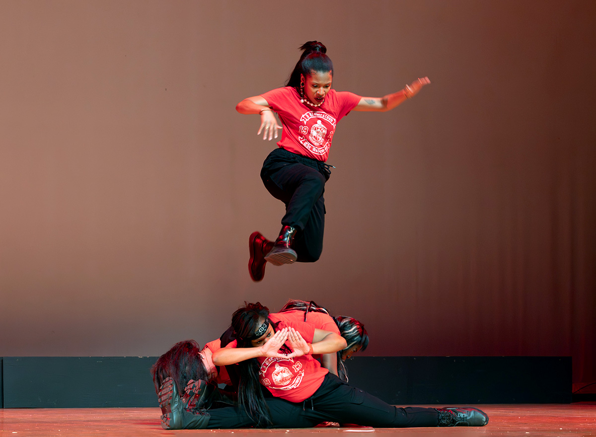 Three women on a stage dressed in red with one jumping in the air