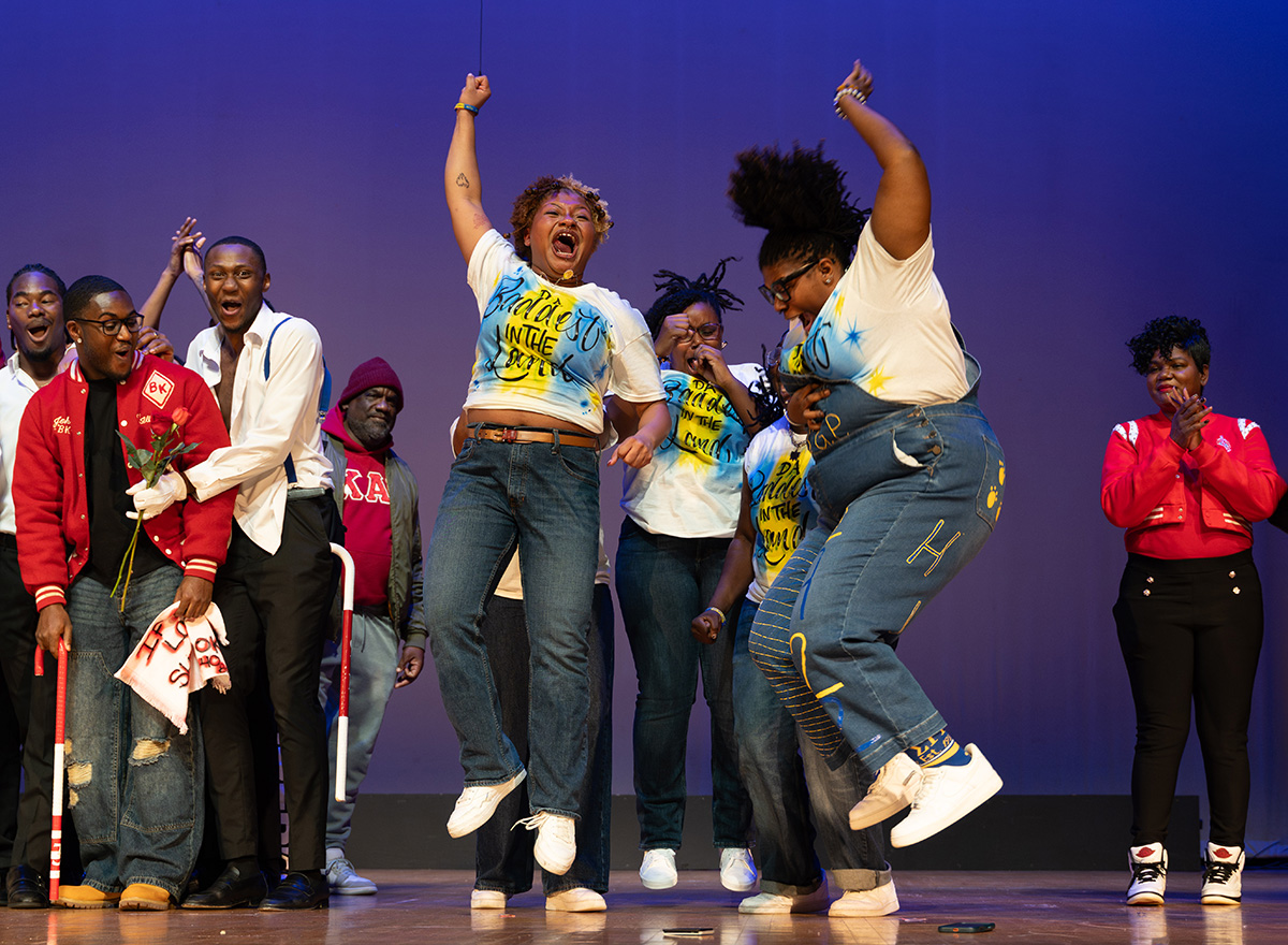 A stage of people with a group of women jumping for joy in the middle