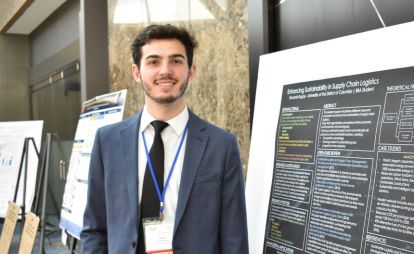 A well-dressed man stands next to a large poster