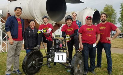 A cheerful group in red shirts poses with a rocket, showcasing teamwork and excitement in a vibrant environment.