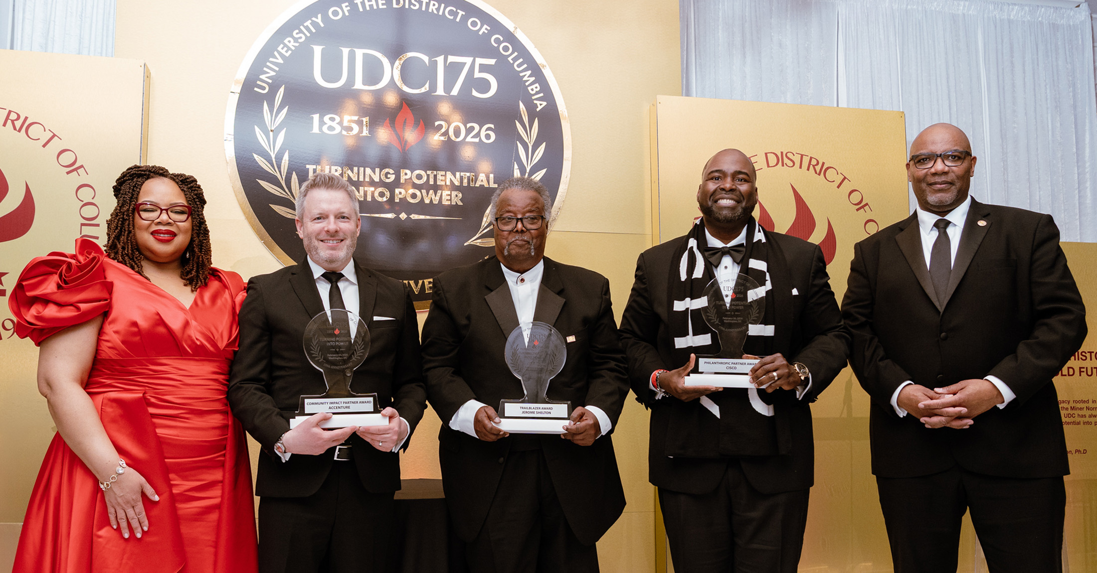 Men standing on a stage, wearing tuxedos and holding awards.