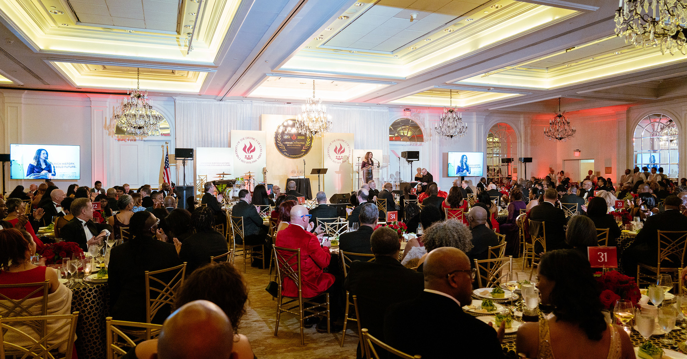 A banquet hall full of people in formal attire, sitting at round tables.
