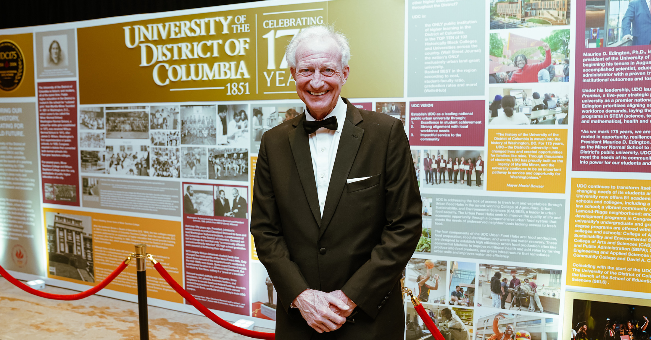 A senior man wearing formal attire, standing and smiling.