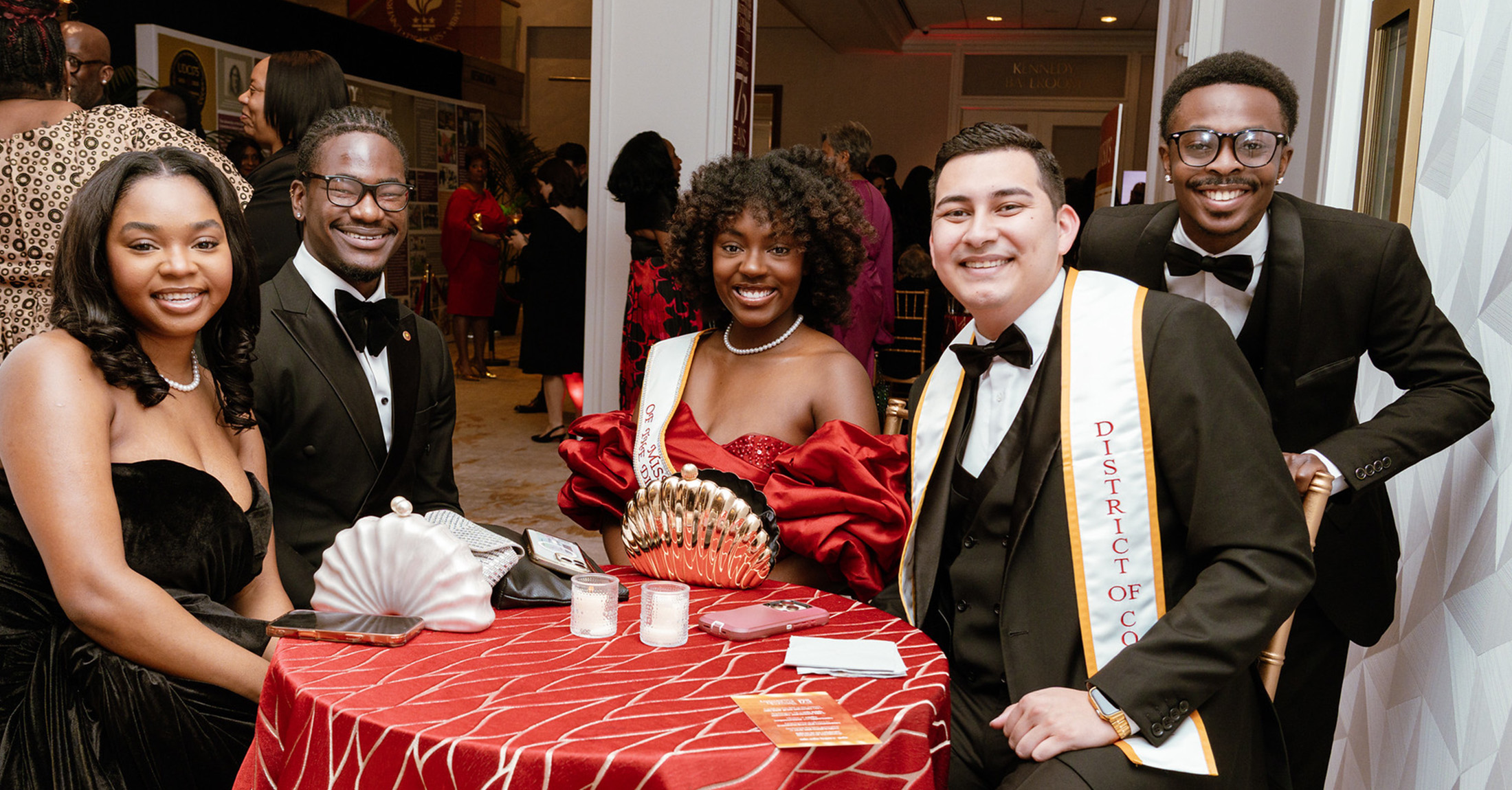 A group of people wearing formal attire sitting at a banquet table and smiling.
