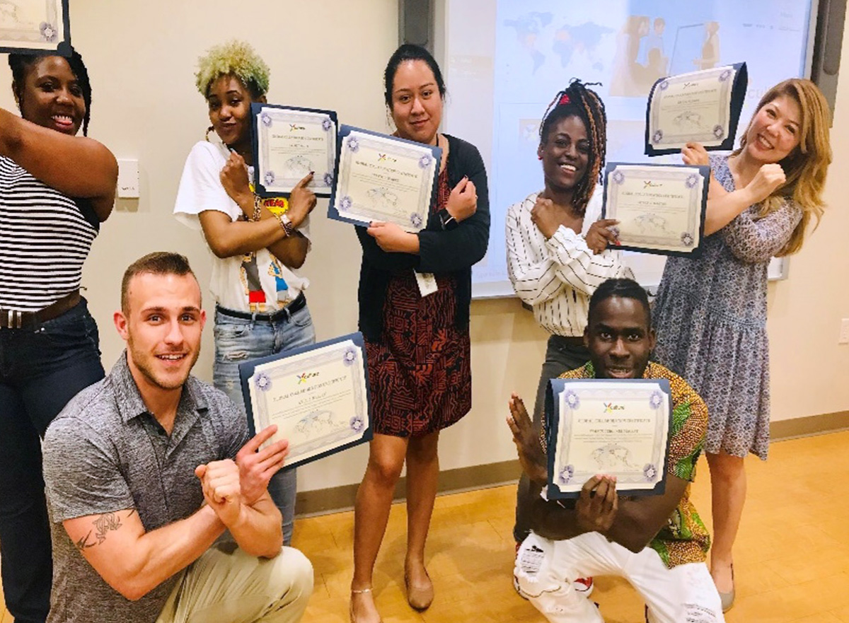 Group of six adults smiling and posing indoors while holding up certificates, as if celebrating a graduation or training completion.