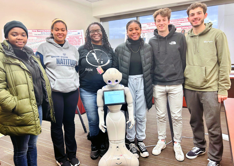 Students standing with a robot in a classroom.