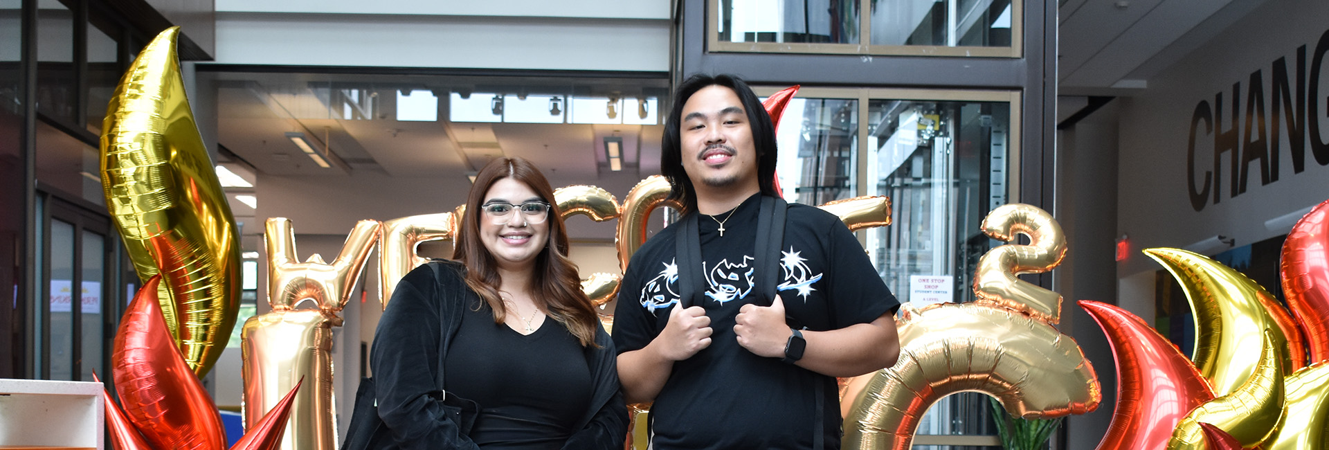 Two UDC students, a woman and a man, standing in front of balloons.