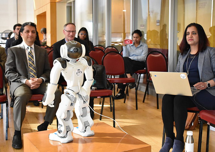 A room of professors sitting and facing a woman holding a laptop