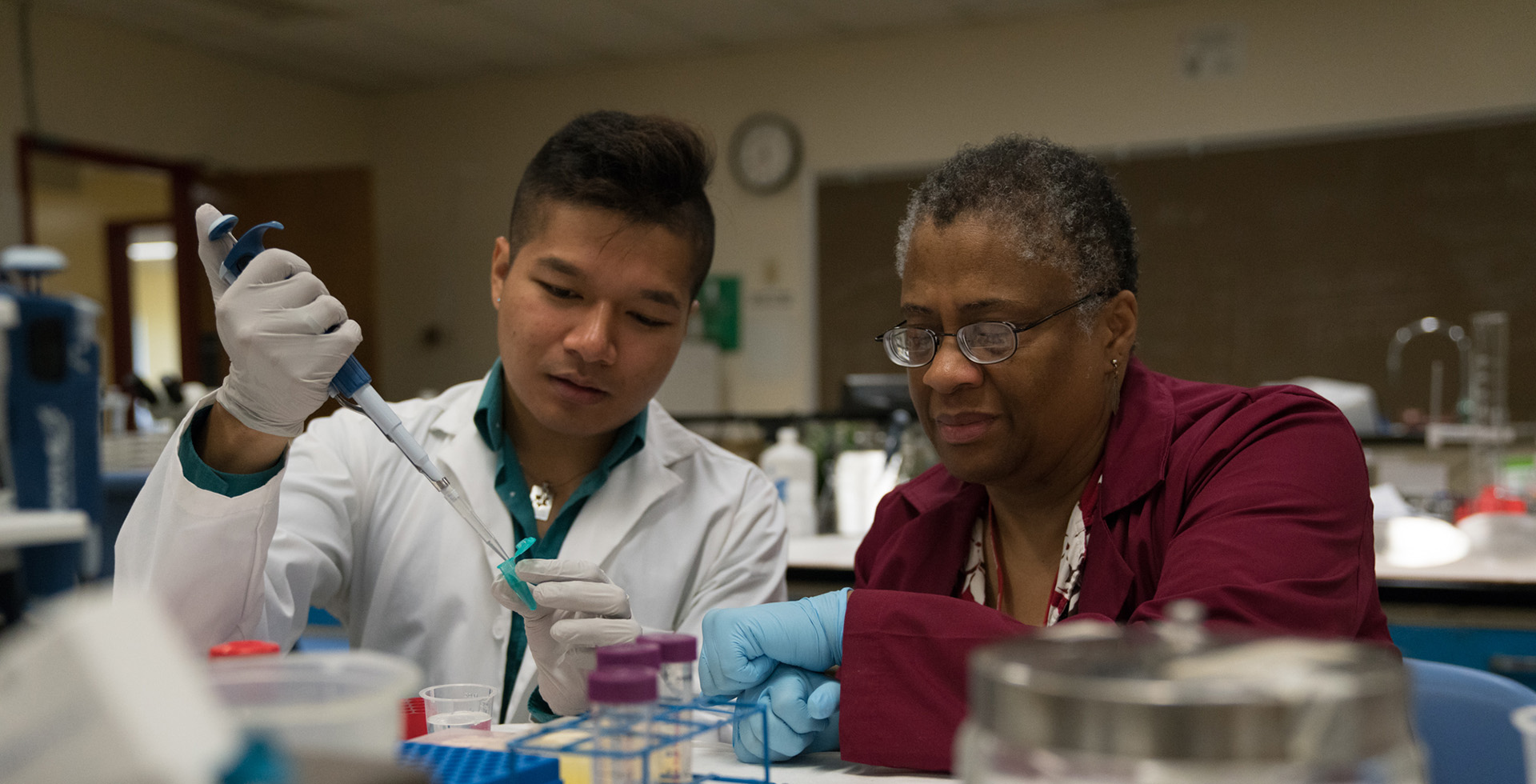 Three faculty standing together and smiling. The man in the middle holds an award.