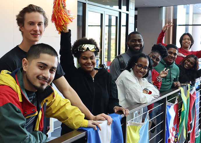 UDC students leaning against a railing holding flags of many countries