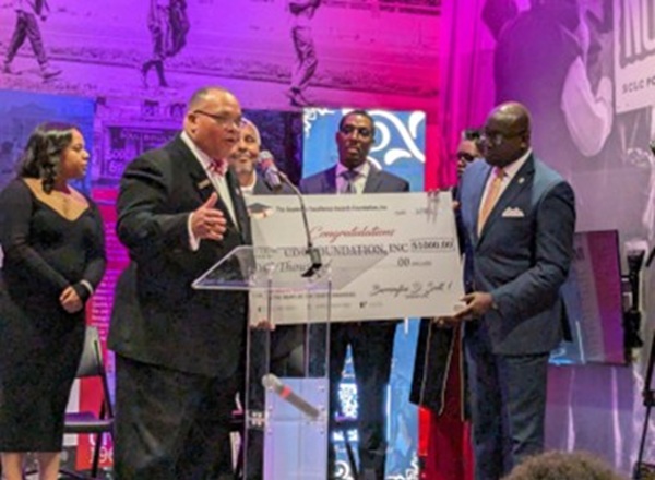 Former UDC Trustee Barrington Scott presents a $1,000 check to the UDC Foundation