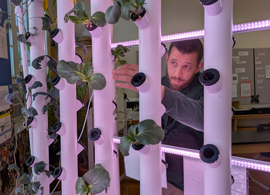 A person tending to a vertical hydroponic garden setup with illuminated grow lights.