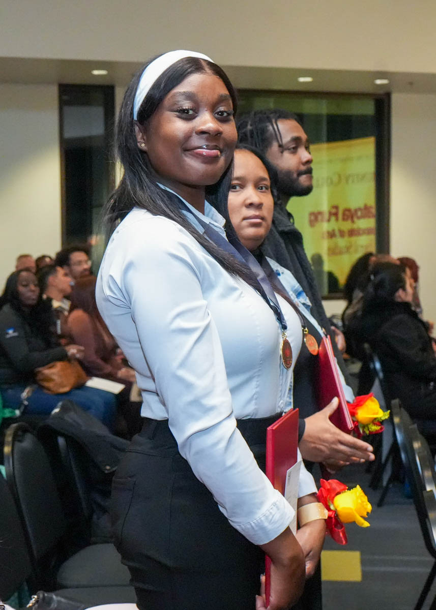 A female college student standing up, looking at the camera and smiling.