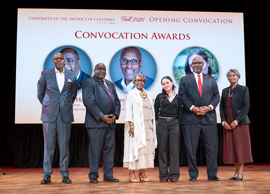 Six award recipients stand on a stage in front of a large screen reading “Convocation Awards” at the University of the District of Columbia Fall 2026 Opening Convocation.