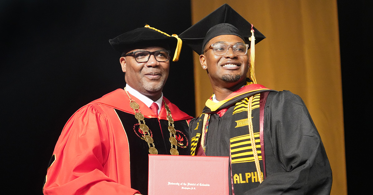 UDC President Maurice D. Edington standing with a graduating student holding a diploma.