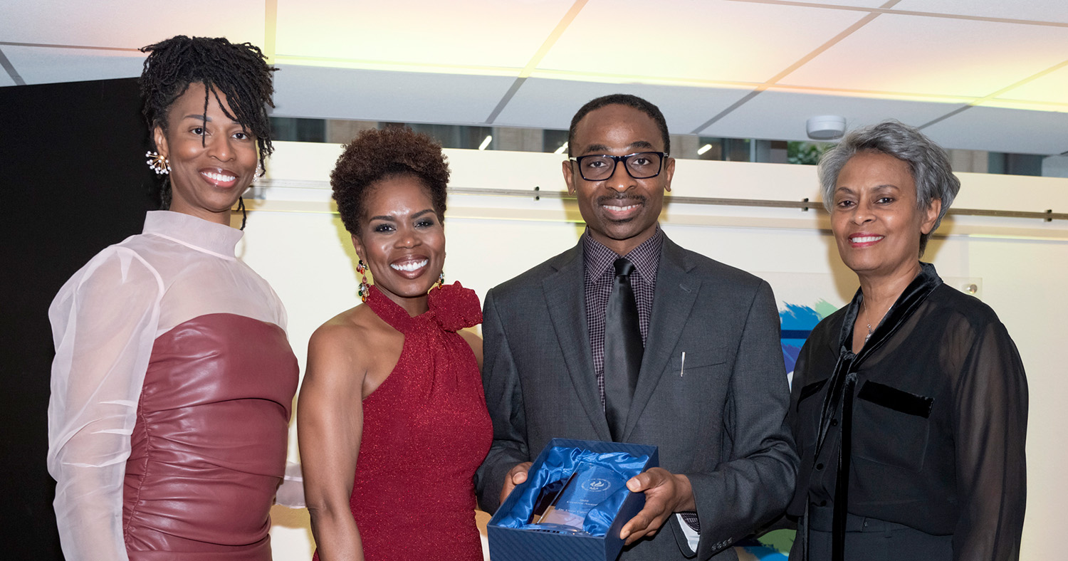 Four people in format attire smiling. One man holds an award.