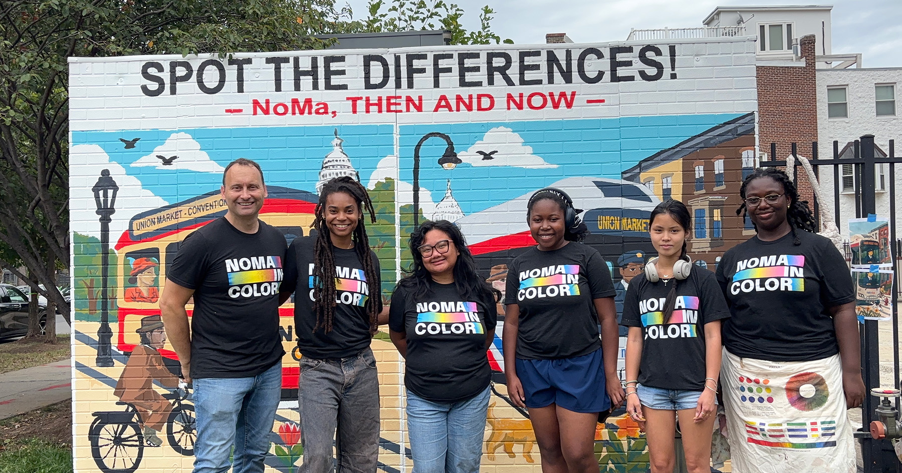 Group of people wearing NoMa in Color t-shirts standing in front of a mural.